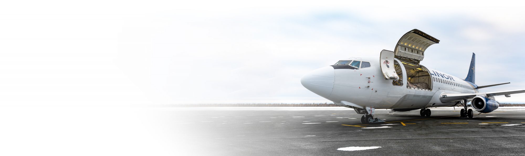 Un avion de ligne avec la porte de chargement ouverte sur un tarmac, prêt à être chargé ou déchargé. Le ciel est clair et l'environnement est hivernal.